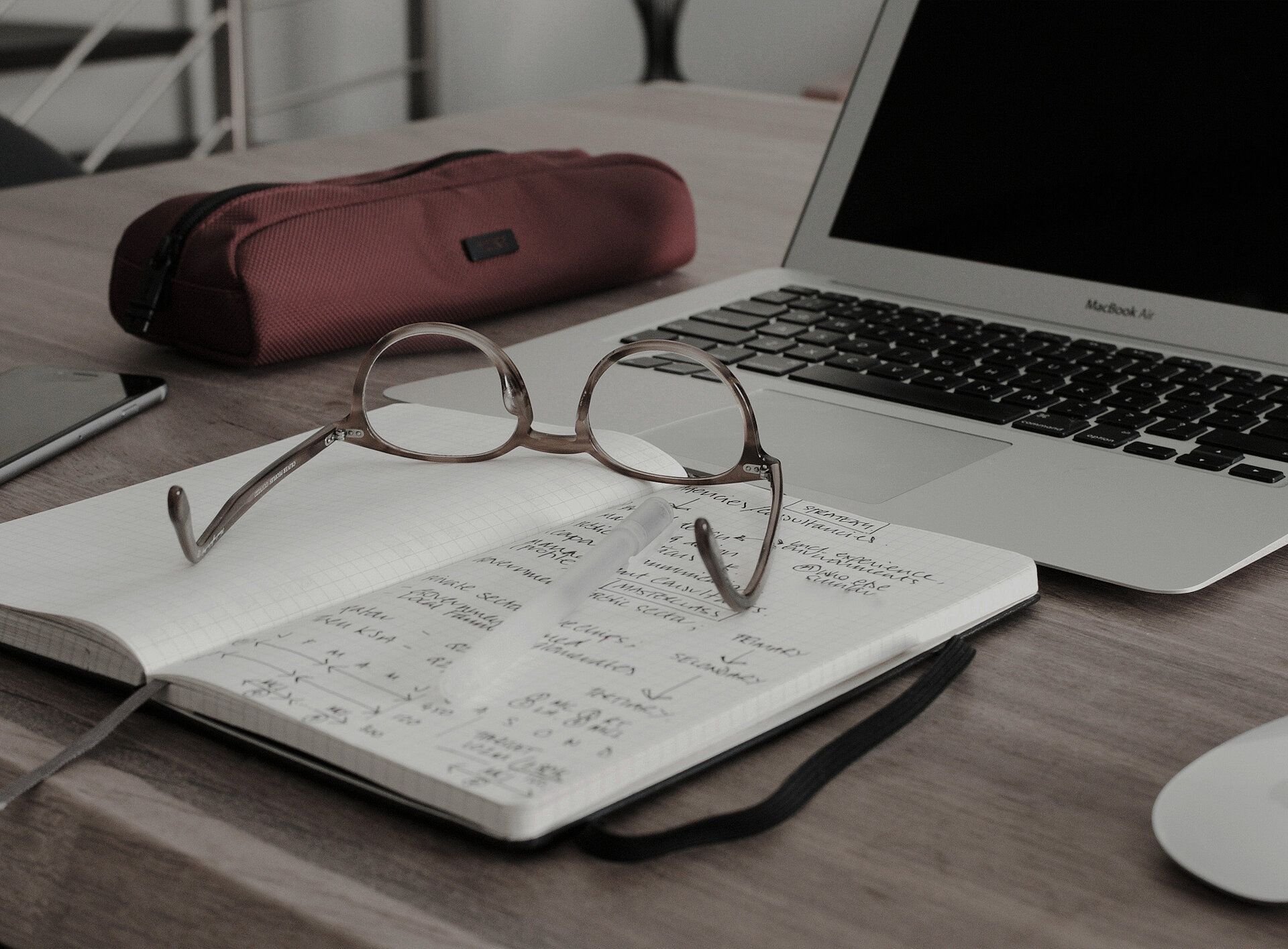 Eine Brille liegt auf einem Buch, im Hintergrund ein Laptop