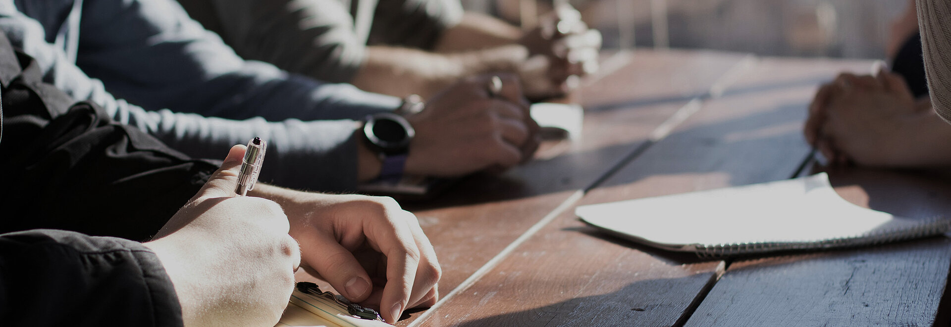 Vier Personen sitzen am Tisch, der Fokus liegt auf ihren Händen