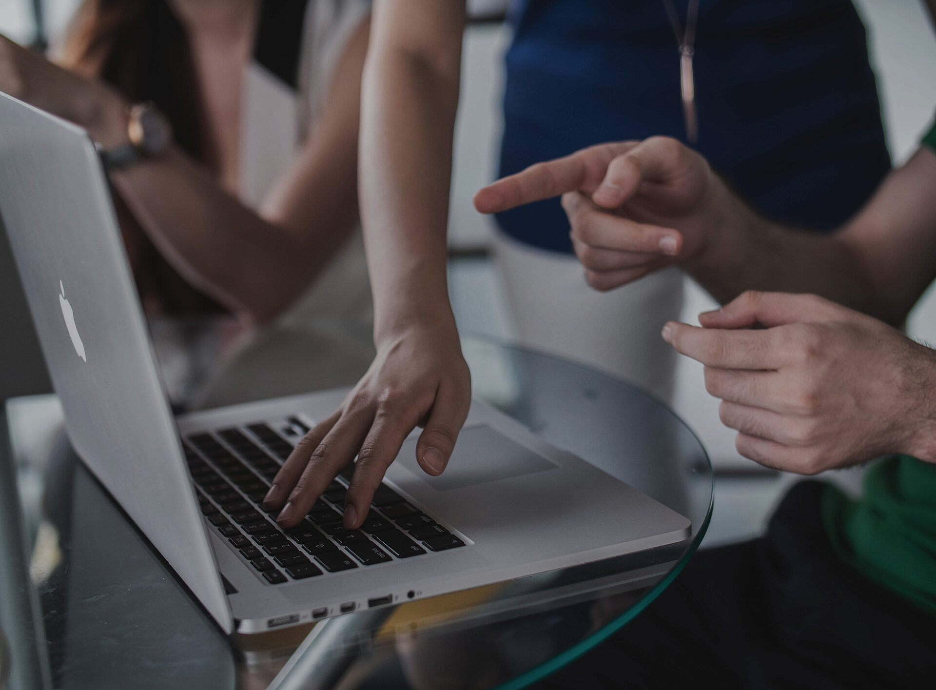 Mehrere Personen stehen um einen Laptop, eine Person zeigt etwas