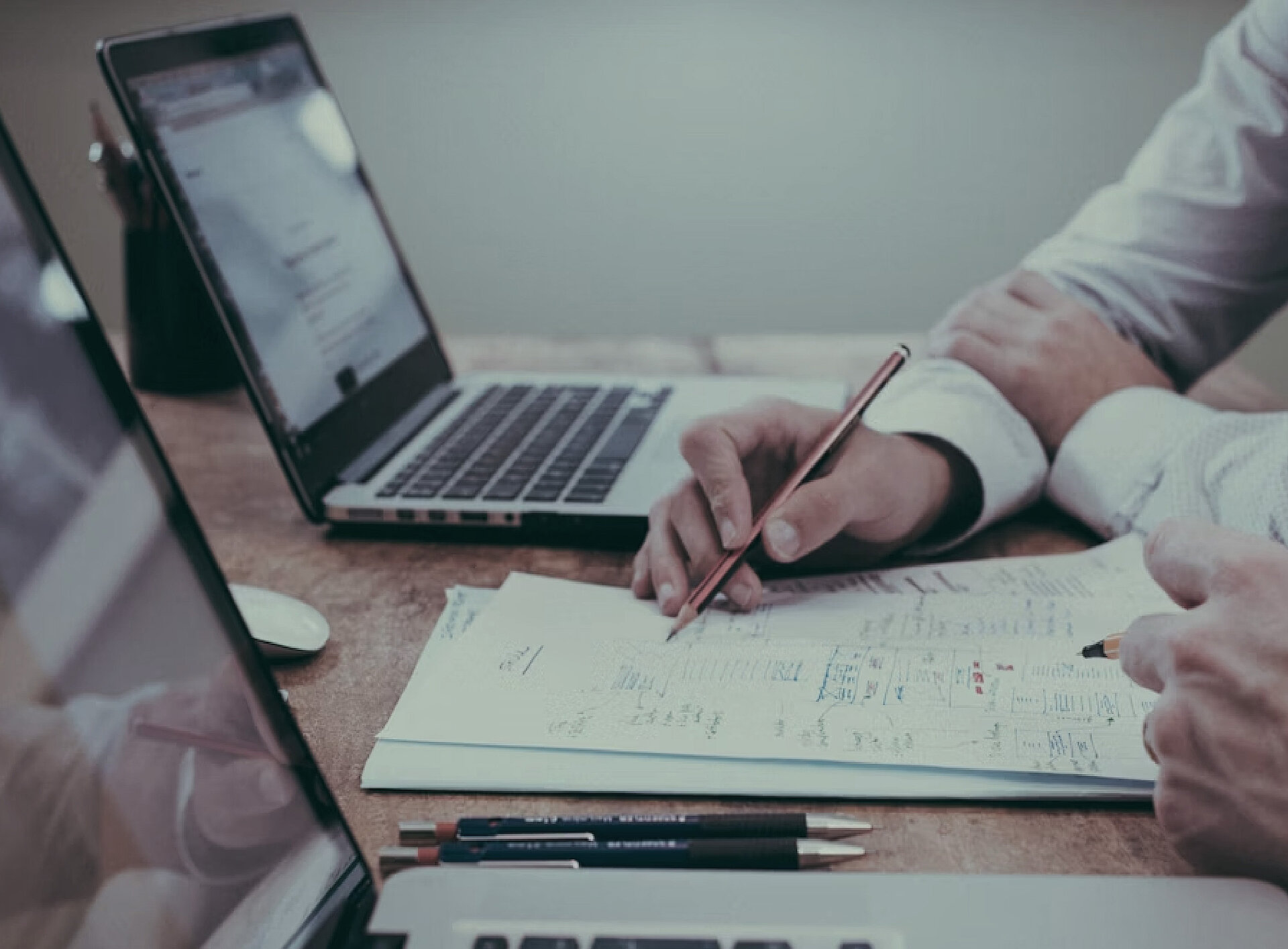 Jemand notiert etwas auf Papier, daneben steht ein Laptop